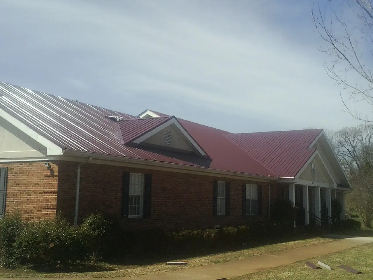 Red metal roof with gabled entries on a long brick building, from a Hail Damage Roof Repair job in Lake Placid