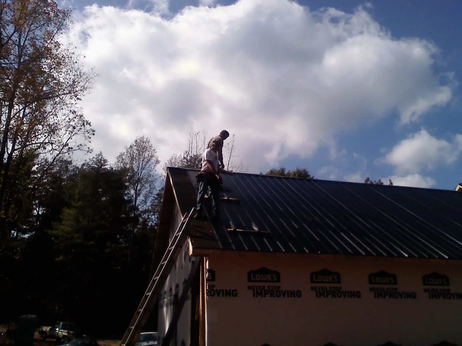 Roofer fastening dark metal panels high against a cloudy sky, from a Roof Inspection job in Lake Placid
