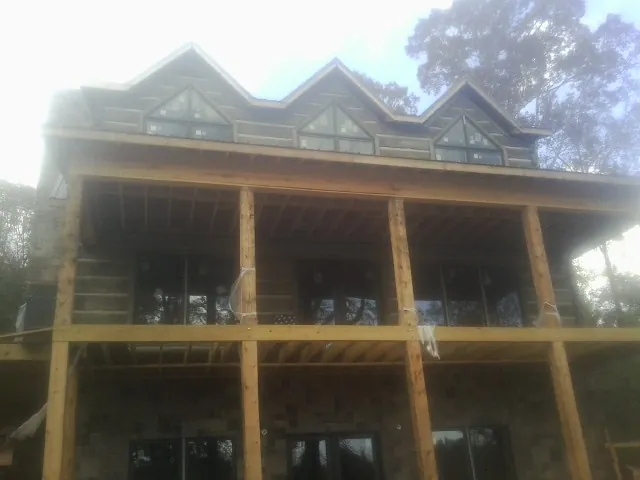 Dormers and porch framing on a large log home under construction — Roof Coating work by our crew in Lake Placid