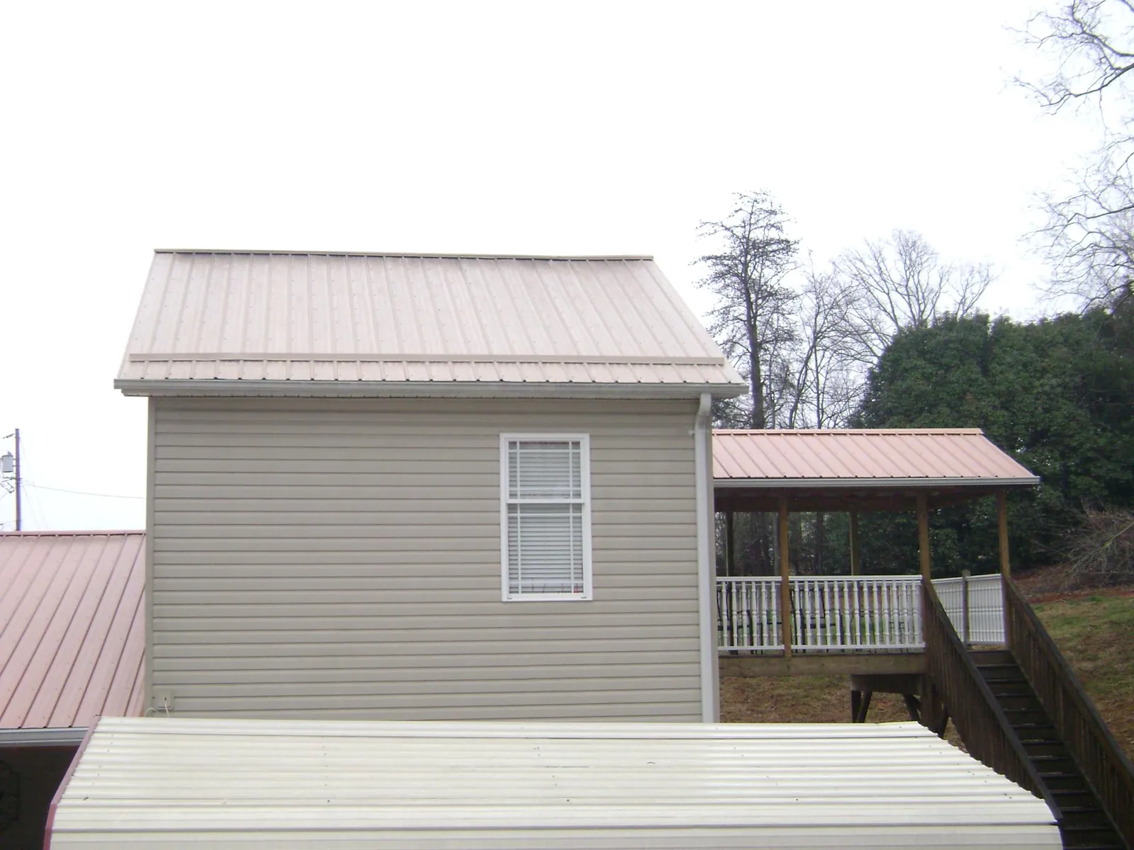 Tan metal roofs on a two story addition and attached porch, from a Roof Replacement job in Lake Placid